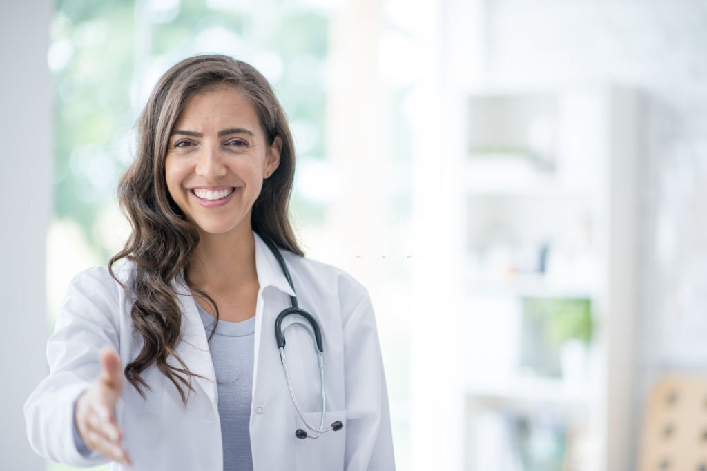 A beautiful female doctor of Hispanic ethnicity is smiling and extending a handshake to a patient.