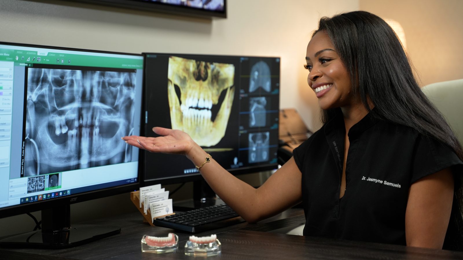 Dr. Jasmyne Samuels reviews 3D dental imaging beside implant and denture models at the Wellness Dental Chandler office