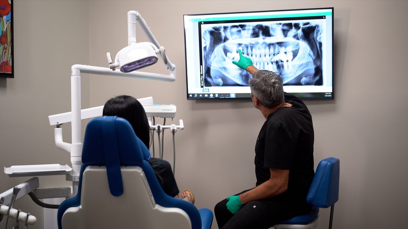 A Wellness Dental doctor points out dental implants on a panoramic X-ray while a patient looks on